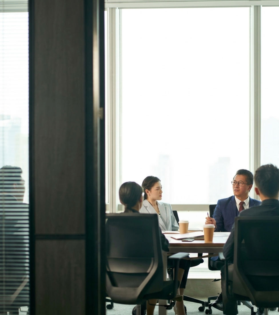 A group of corporate professionals sitting around a conference table in a modern office, engaged in a discussion